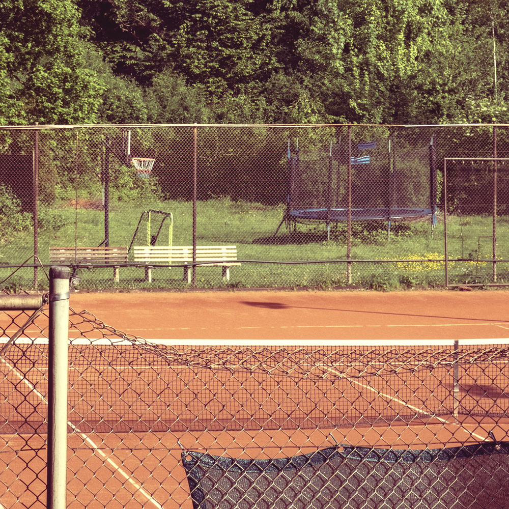 Ausblick auf einen Tennisplatz, daneben und dahinter liegen grüne Flächen