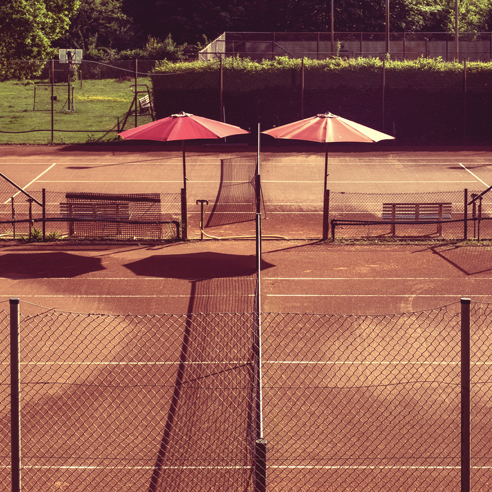 Blick auf einen Tennisplatz mit einem grünen Bereich im Hintergrund und an der Seite