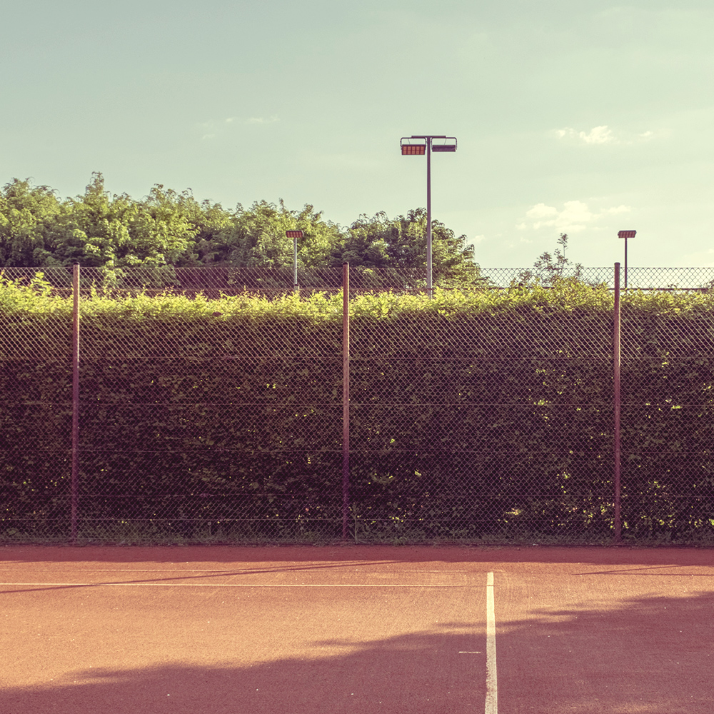 Ausblick auf einen Tennisplatz, daneben und dahinter liegen grüne Flächen