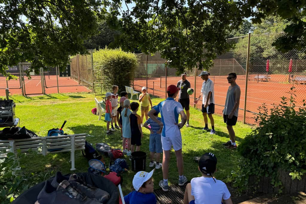 Kinder wärmen sich vor dem Spiel auf, umgeben von einem Tennisplatz und einer frischen, offenen Atmosphäre