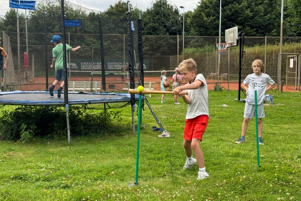 Kinder spielen neben dem Tennisplatz, umgeben von Grün und frischer Luft