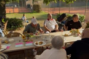 Mitglieder des TC Forstwald sitzen beim Kartoffelcup 2026 an einem Terrassentisch mit Sonnenblumen, Kartoffeln und Essen