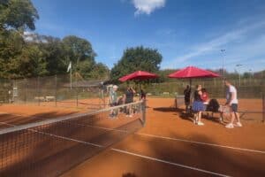 Mitglieder des TC Forstwald stehen am Netz neben roten Sonnenschirmen auf dem Platz beim Kartoffelcup 2026